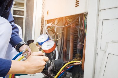 Technician sitting and checking HVAC system unit outside home