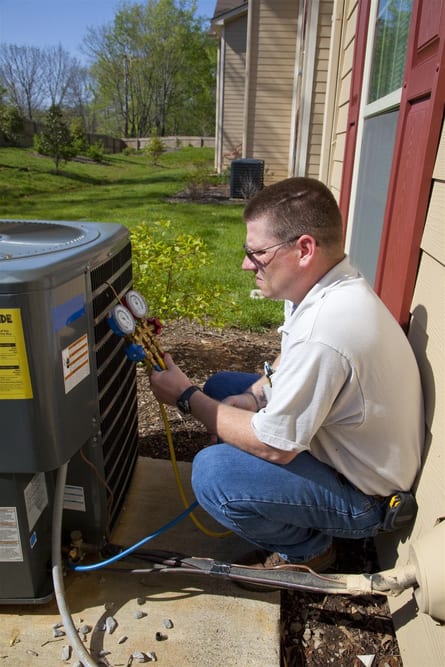 Technician sitting and checking HVAC system unit outside home